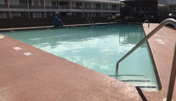 An outdoor swimming pool at a motel with a handrail for steps leading into the water. There are buildings and mountains in the background.