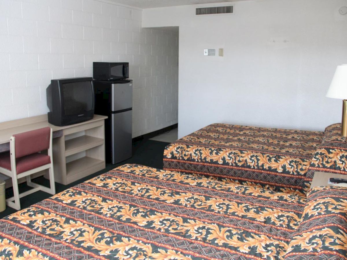 This image shows a motel room with two beds, a desk with a chair, a small TV, a mini-fridge, and a lamp on the desk.