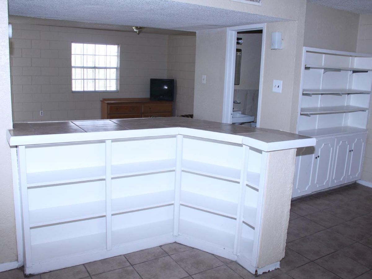 A room with white shelves and cabinets, a window, a TV in the corner, and tiled flooring.