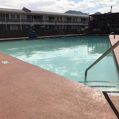 An outdoor swimming pool is in the foreground, with a few lounge chairs and a motel building in the background. Mountains are visible in the distance.