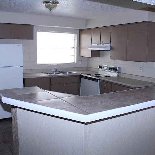 A modern kitchen featuring a tiled countertop, white fridge, stove, dishwasher, and ample cabinet space under good lighting.