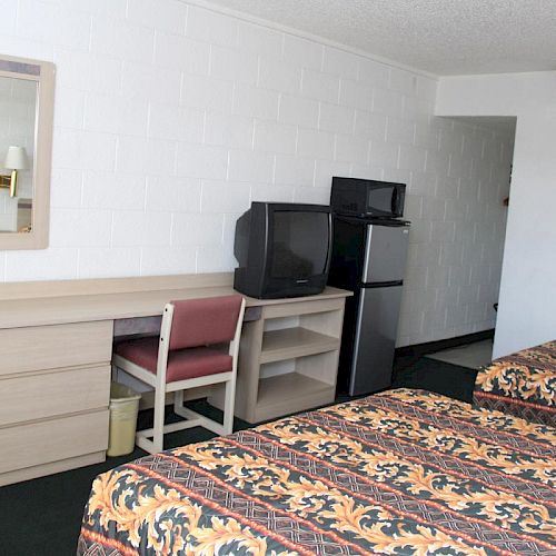 A hotel room with two beds, a desk with a TV, a mini fridge, a mirror, a chair, and a waste bin underneath the desk.