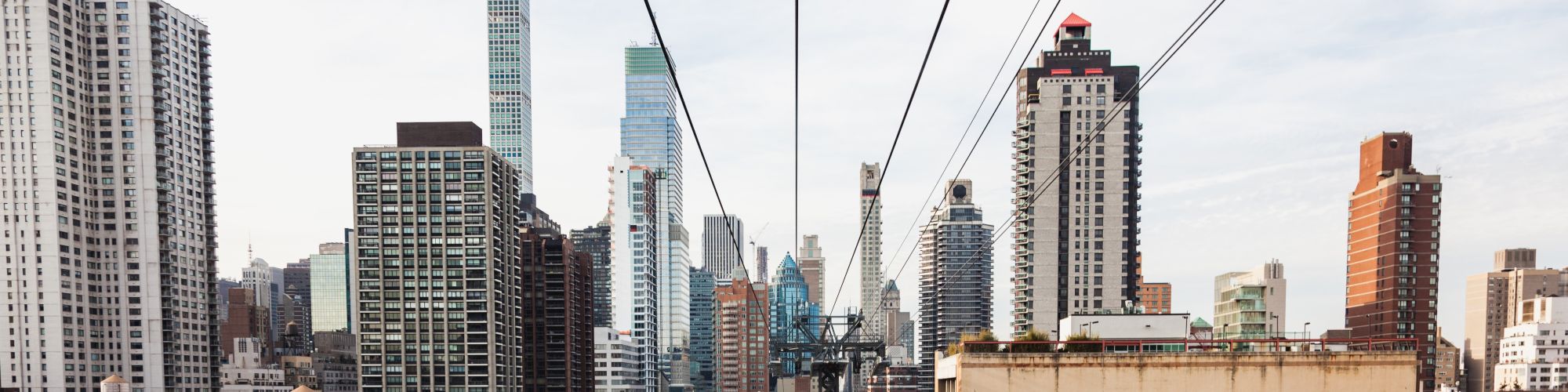 A cityscape featuring numerous skyscrapers under a clear sky with cables running through the foreground, possibly from a bridge or tram system ending the sentence.